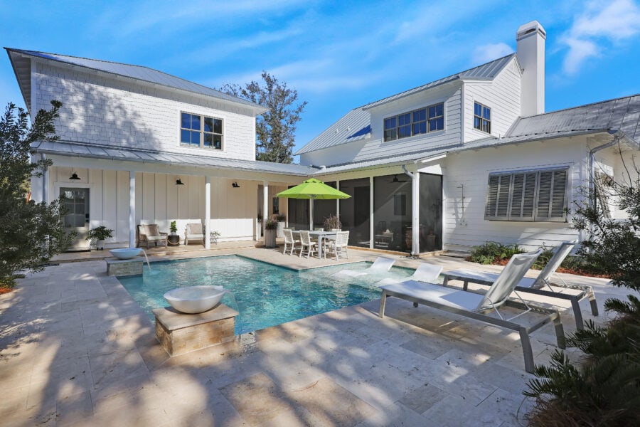 Modern white house with a backyard swimming pool, outdoor seating area, and lush landscaping under a bright blue sky.