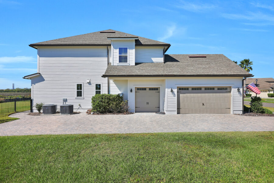 Modern white two-story home with a spacious driveway, attached garage, well-manicured lawn, and American flag near the entrance, showcasing attractive exterior design and landscaping.