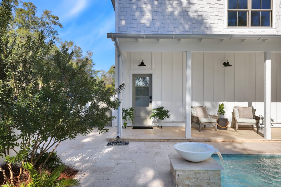 Modern white house exterior with a cozy porch, outdoor seating, lush greenery, and a water fountain, perfect for relaxing and enjoying outdoor living.