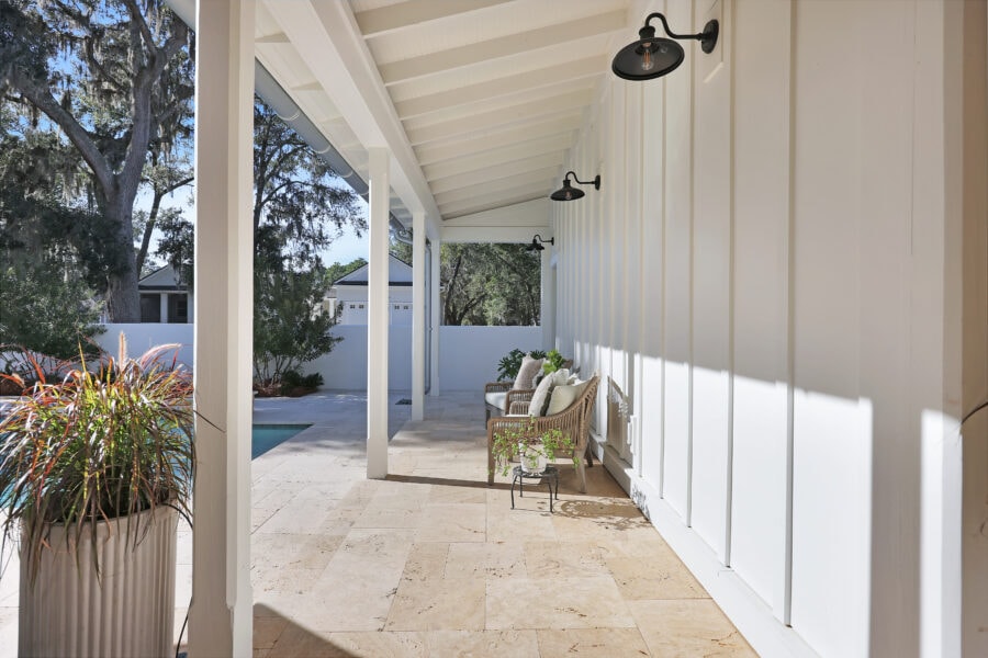 Modern covered outdoor patio with white exterior walls, black wall-mounted outdoor lights, and cozy seating area surrounded by lush greenery.