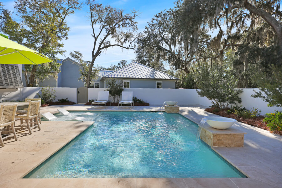 Luxurious backyard with a sparkling in-ground pool, surrounded by outdoor seating, lush trees, and a white privacy fence, perfect for relaxation and entertaining.