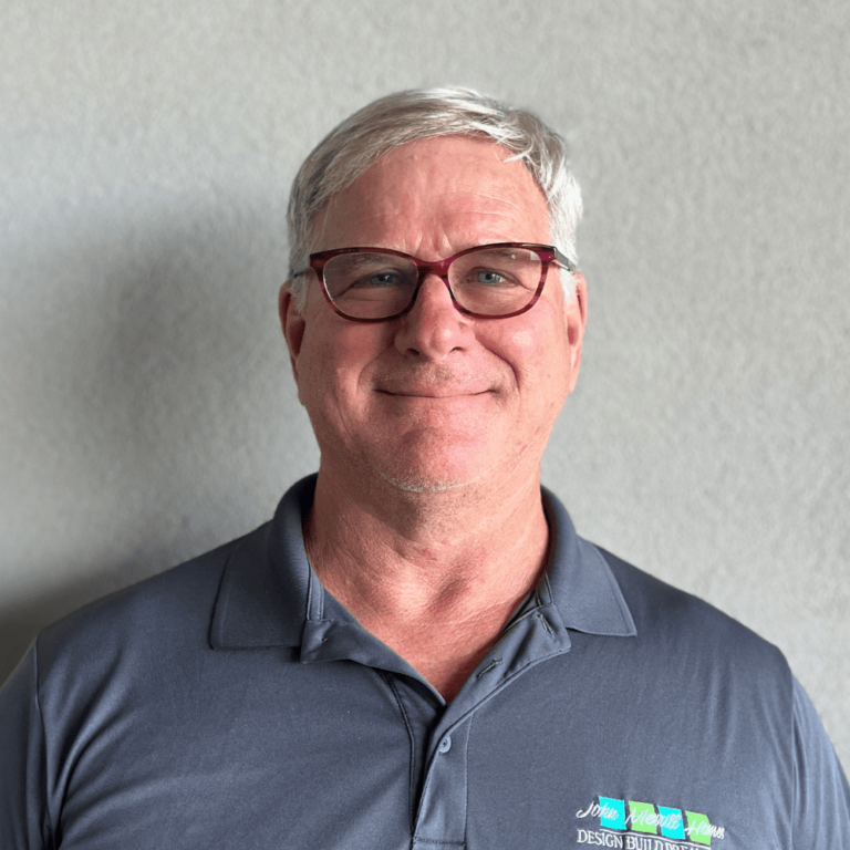Custom home builder smiling in front of a light wall, wearing branded polo shirt.
