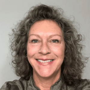 Modern woman smiling, short curly hair, casual attire, indoor setting, friendly professional appearance, marketing for John Merrill Homes.