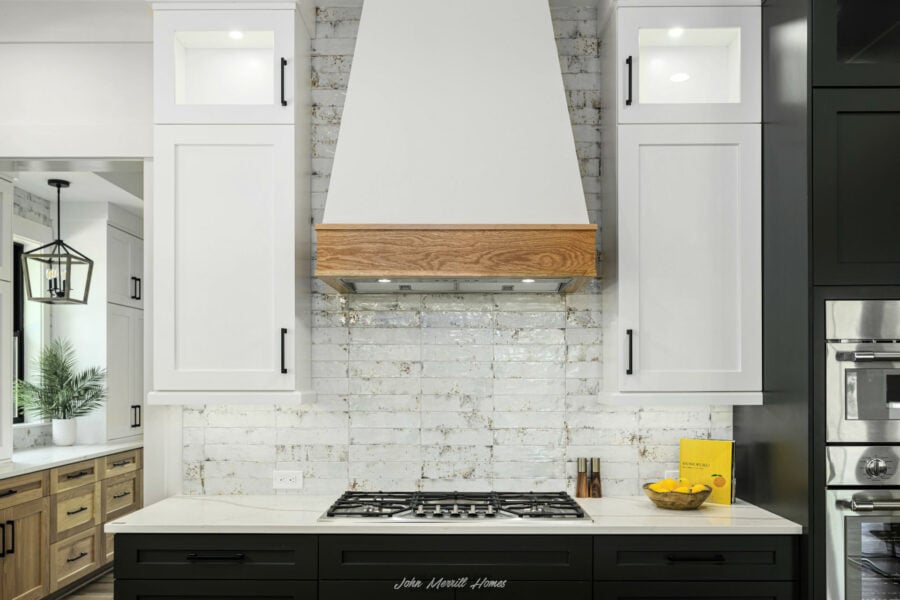 Modern kitchen with white and black cabinetry, a stainless steel range, a white countertop, and a stylish white brick backsplash with a wooden accent on the range hood.