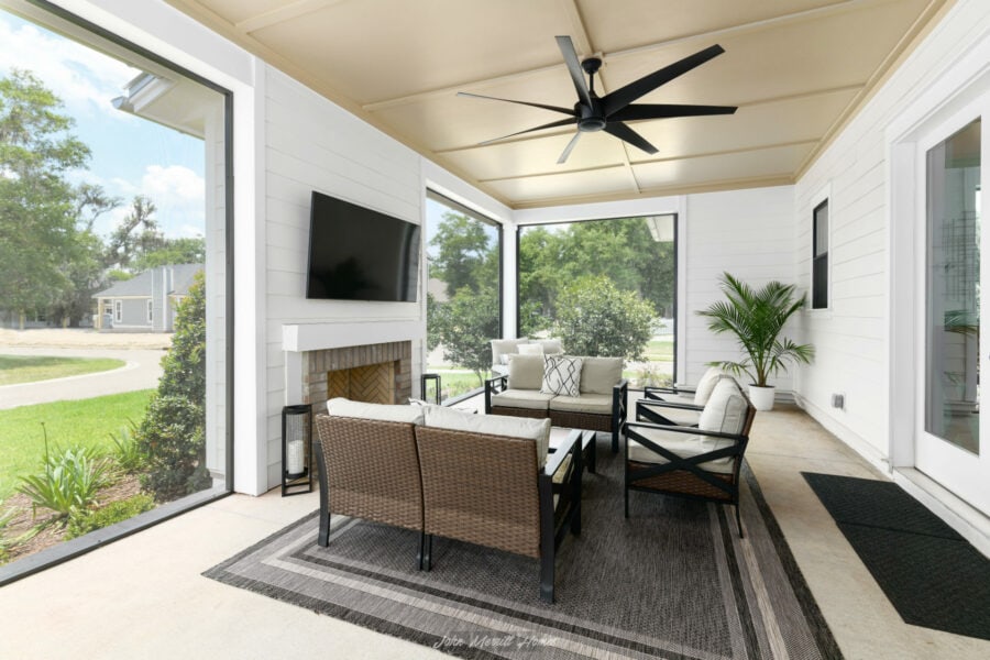 Spacious screened-in porch with comfortable seating, ceiling fan, and fireplace, overlooking lush green yard with trees and neighborhood homes in the background.