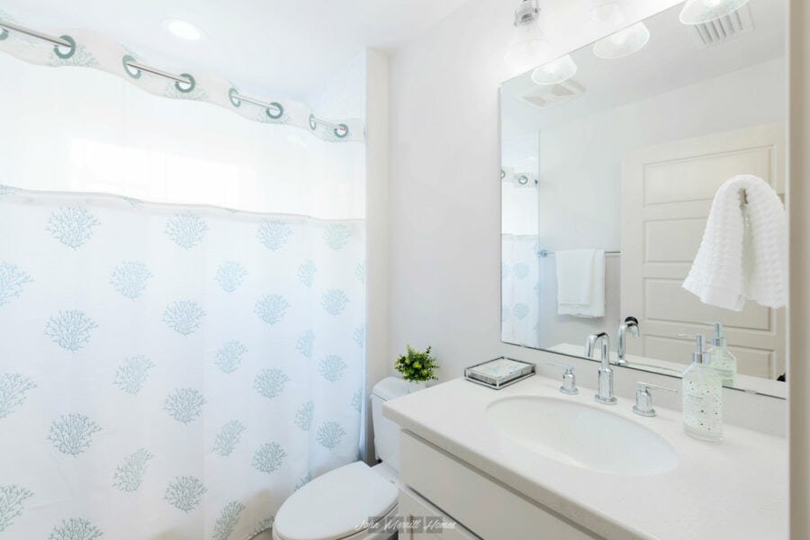 Modern white bathroom with a shower curtain featuring blue coral designs, a large mirror above a white vanity, and contemporary fixtures, creating a bright and clean space.
