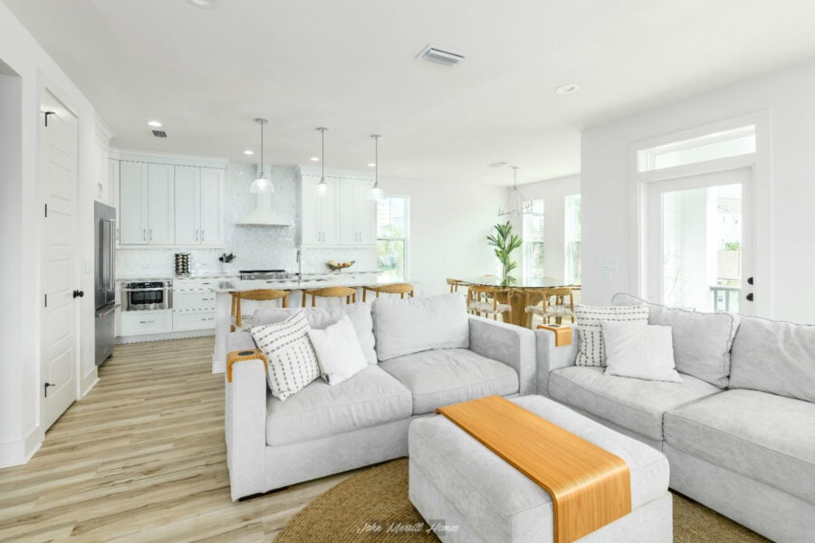Modern open-concept living room with bright white walls, cozy sectional sofa, and large windows for natural light, seamlessly connected to a stylish kitchen and dining area.