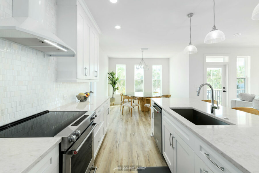 Bright, modern kitchen interior featuring white cabinetry, marble countertops, stainless steel appliances, and a spacious open-concept layout with natural light.