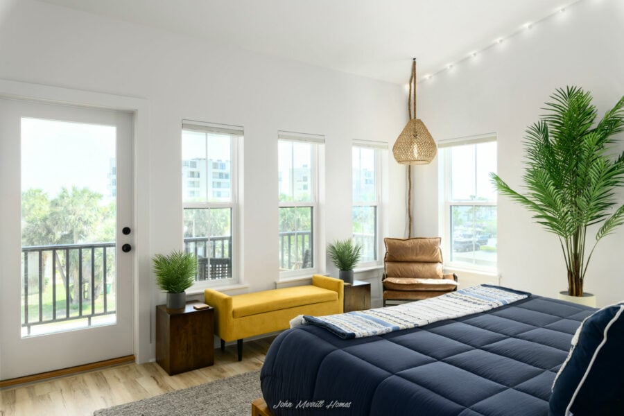 Modern bedroom with large windows, cozy furniture, indoor plants, and stylish decor, creating a bright and inviting atmosphere.