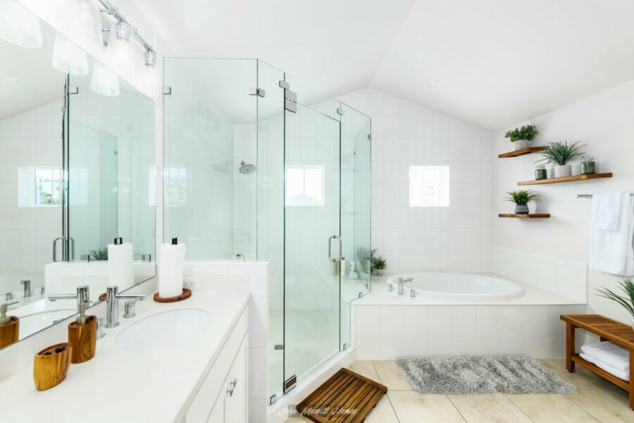 Bright and modern white bathroom featuring a spacious glass-enclosed shower, a built-in bathtub, wooden accents, and stylish wall-mounted shelves with potted plants, creating a relaxing and inviting space.