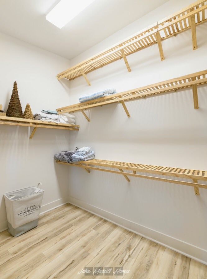 Clothing storage in a walk-in closet with wooden shelves and neatly folded clothes, minimalist design, bright lighting, light wood flooring.