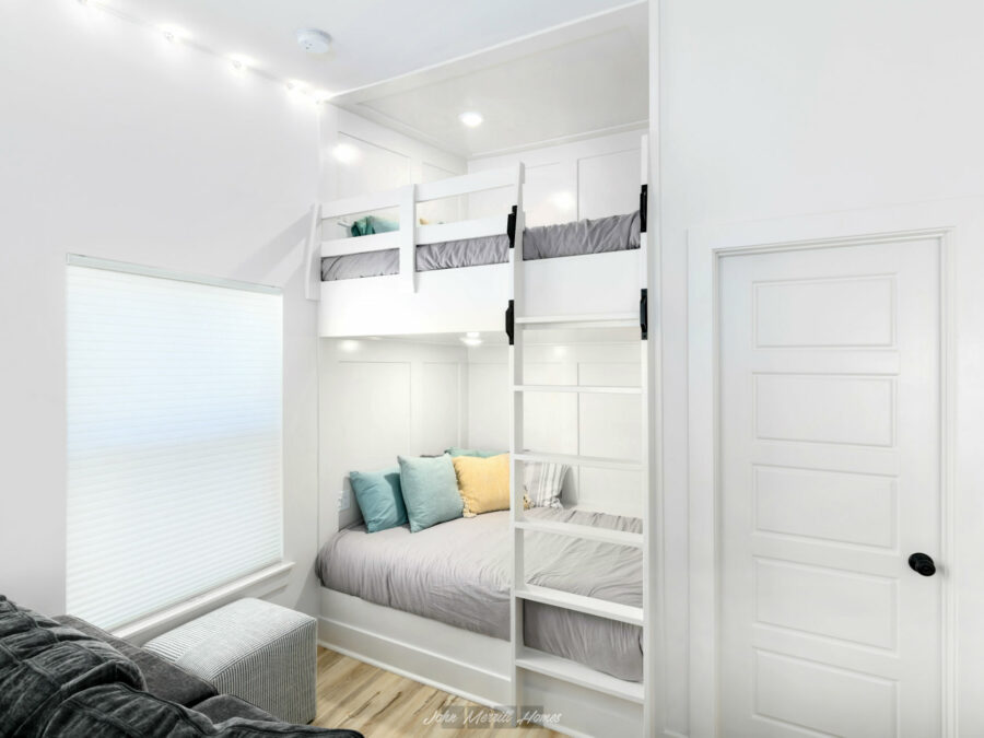 Bright, modern bedroom featuring a built-in bunk bed with a lower full-size bed and an upper twin bed, all finished in white with cozy bedding and decorative pillows; natural light streaming through a large window.