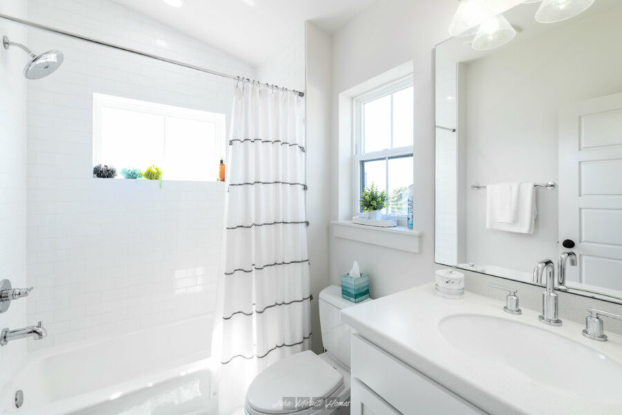 Bright white bathroom with a bathtub, showerhead, window, vanity with sink, mirror, and modern fixtures in a new home.