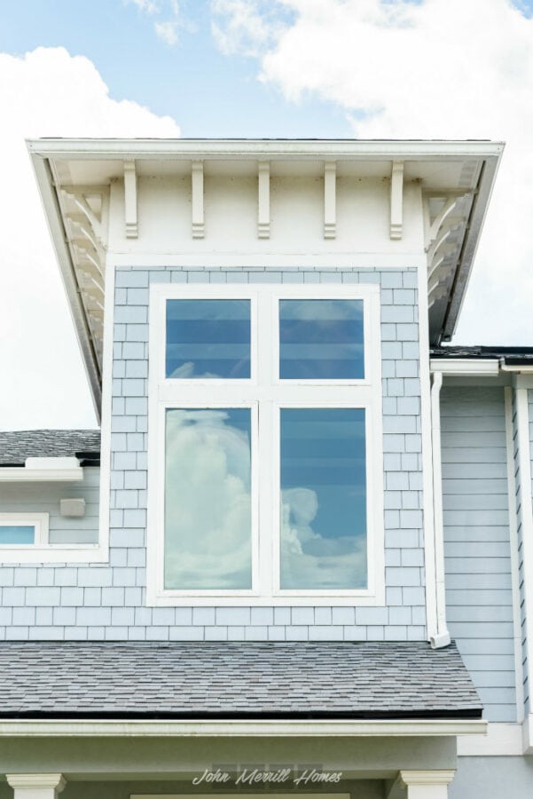 Modern blue and white cottage-style home exterior featuring large multi-pane windows, shingle siding, and decorative trim under a bright sky.