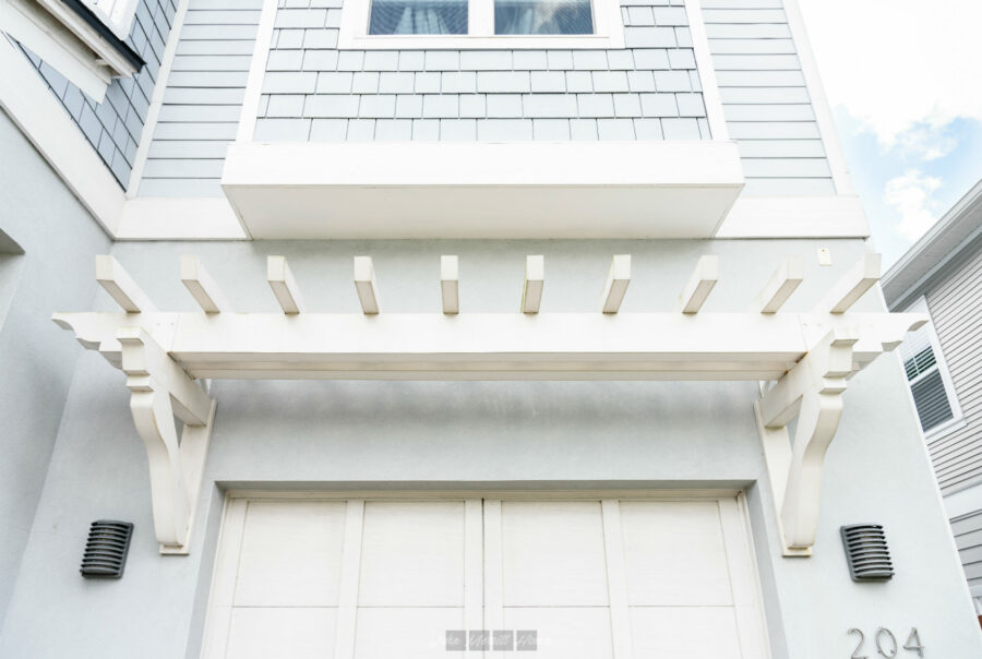 Elegant white exterior architecture featuring a decorative pergola and modern design elements at John Merrill Homes.