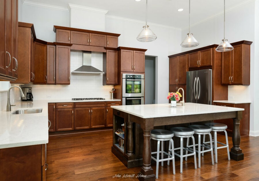 Spacious kitchen with warm wooden cabinets, white countertops, and a large island with seating, modern stainless steel appliances, and pendant lighting, perfect for cooking and entertaining.