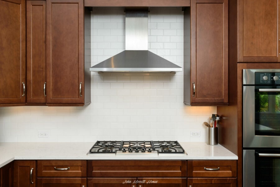 Stylish kitchen featuring rich wooden cabinets, a modern stainless steel range hood, and a built-in oven, creating a warm and contemporary cooking space.