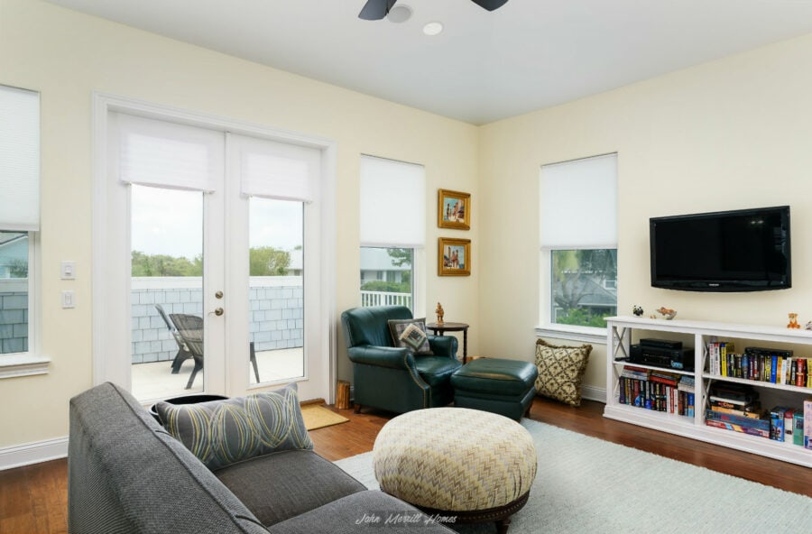 Cozy living room with a gray sofa, green leather chair with ottoman, white entertainment center, and large windows providing natural light in a modern home.
