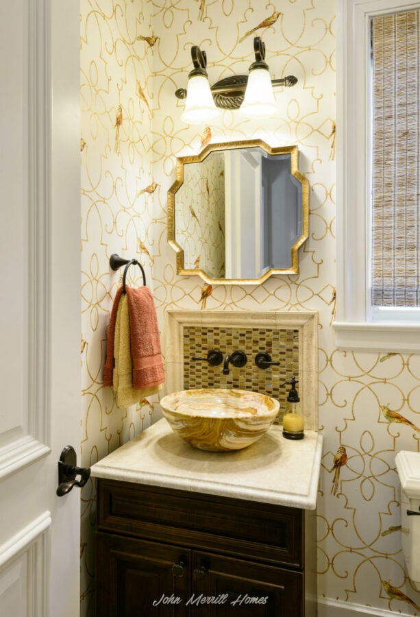 Vibrant bathroom with bird-themed wallpaper, a decorative mirror with gold accents, a vessel sink made of patterned stone, dark wood cabinetry, and modern fixtures, creating an elegant and inviting space.
