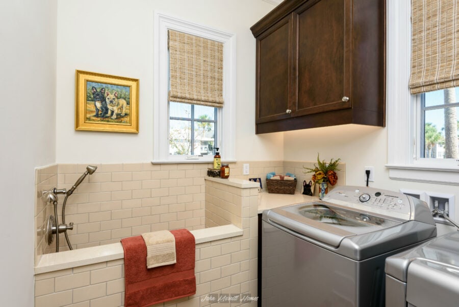 Bright laundry room featuring a utility sink, washing machine, dark wood cabinets, and natural light from windows with bamboo blinds.