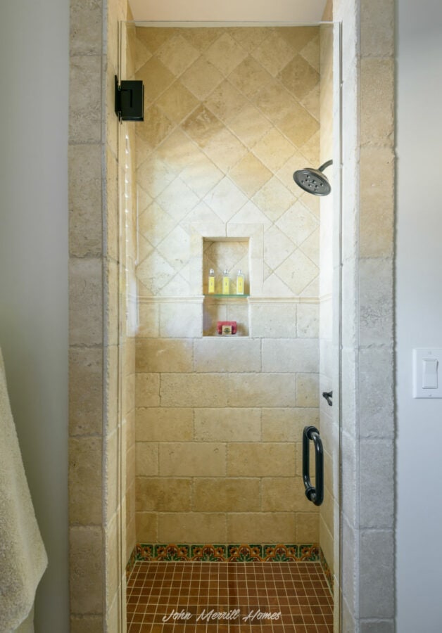 Stone tile walk-in shower with a built-in niche, black showerhead, and glass door handle, featuring decorative tile accents at the base.