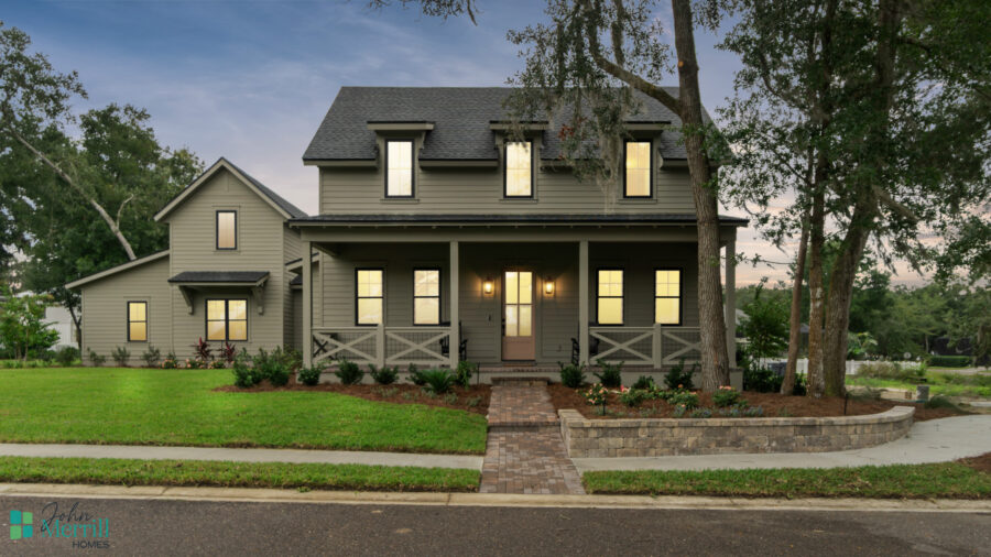 Luxurious Modern Home with Grey Siding and a Front Porch Surrounded by Well-Manicured Lawn and Mature Trees at Dusk.