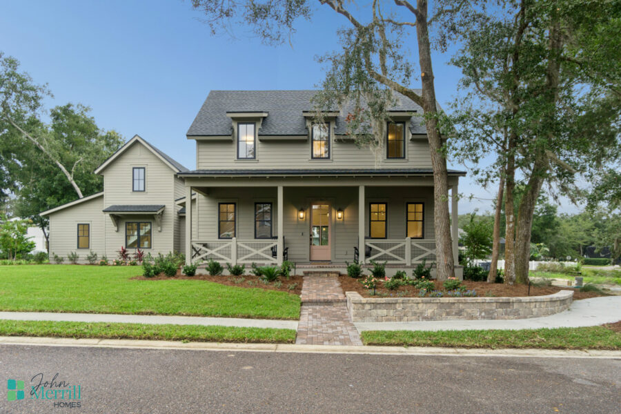 Luxurious modern two-story house with a spacious front porch, surrounded by lush greenery and landscaped garden, showcasing timeless design by John Merrill Homes.