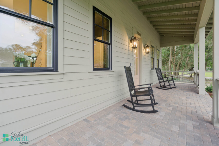 1. Beautiful front porch of a modern American home featuring cozy black rocking chairs, exterior lighting, and a view of lush greenery, perfect for relaxing outdoors.
