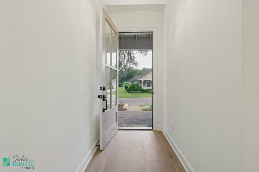 Bright, modern entryway with white walls, light wood flooring, and a glass-paneled door opening to a landscaped front yard and neighborhood.