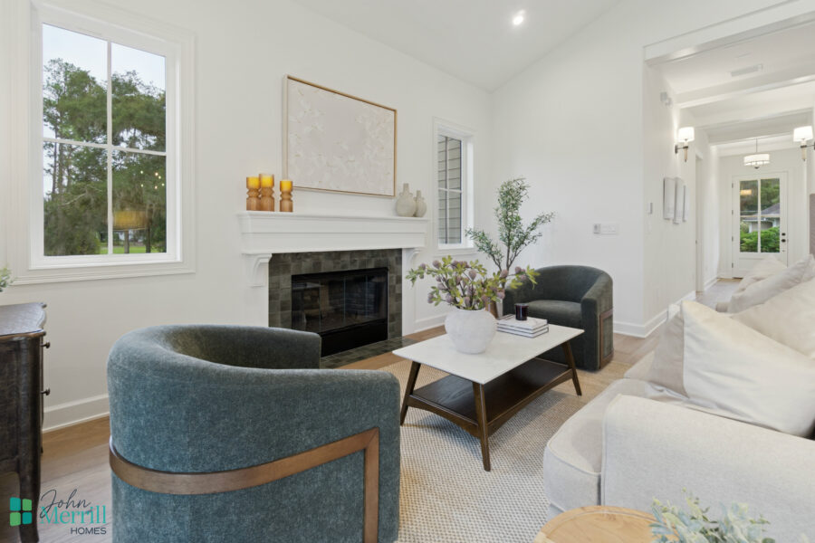 1. Bright living room interior with white walls, large windows, cozy seating, a fireplace, and elegant decor, showcasing modern home design by John Merrill Homes.