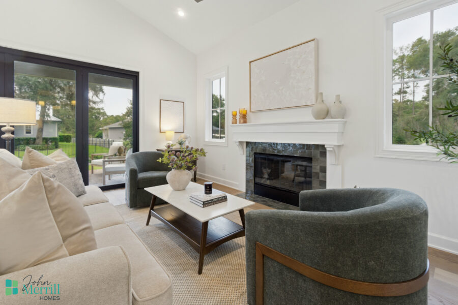 1. Bright living room with white walls, gray upholstered chairs, a beige sofa, and a modern fireplace with decorative vases and artwork, overlooking an outdoor patio through large windows and sliding doors.