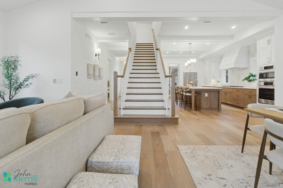 Bright open-concept living room and kitchen in a modern home with white walls, wooden flooring, and elegant furnishings, showcasing a spacious and inviting interior design.