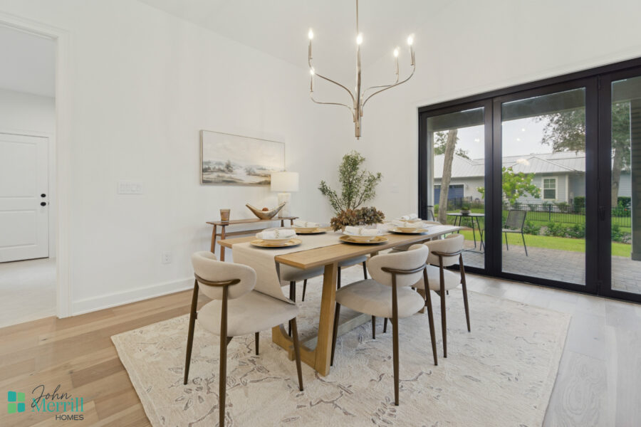 Bright and modern dining area with large sliding glass doors opening to a backyard patio, featuring a stylish chandelier, neutral tones, and elegant table setting for family gatherings.