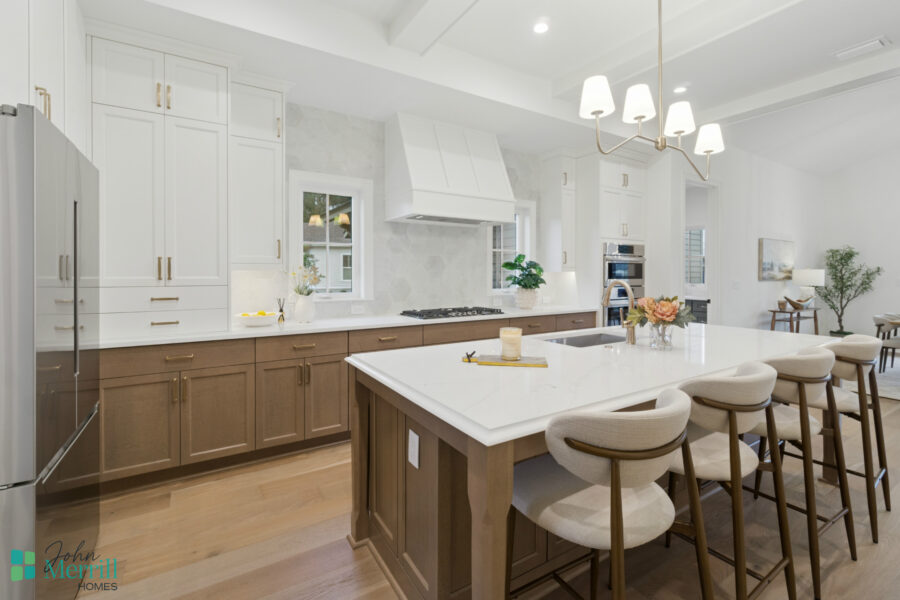 Modern kitchen with white and wood cabinetry, an island with seating, stainless steel appliances, and elegant lighting in a spacious, bright open-concept home.