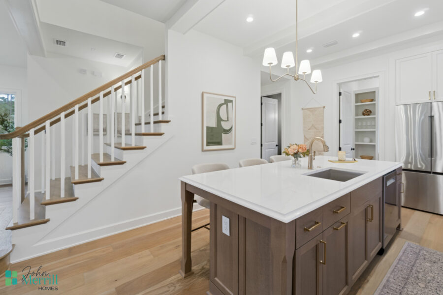 Bright, modern kitchen with white cabinetry, a large white quartz island, stainless steel appliances, and elegant lighting fixtures, creating a welcoming space for cooking and gatherings.