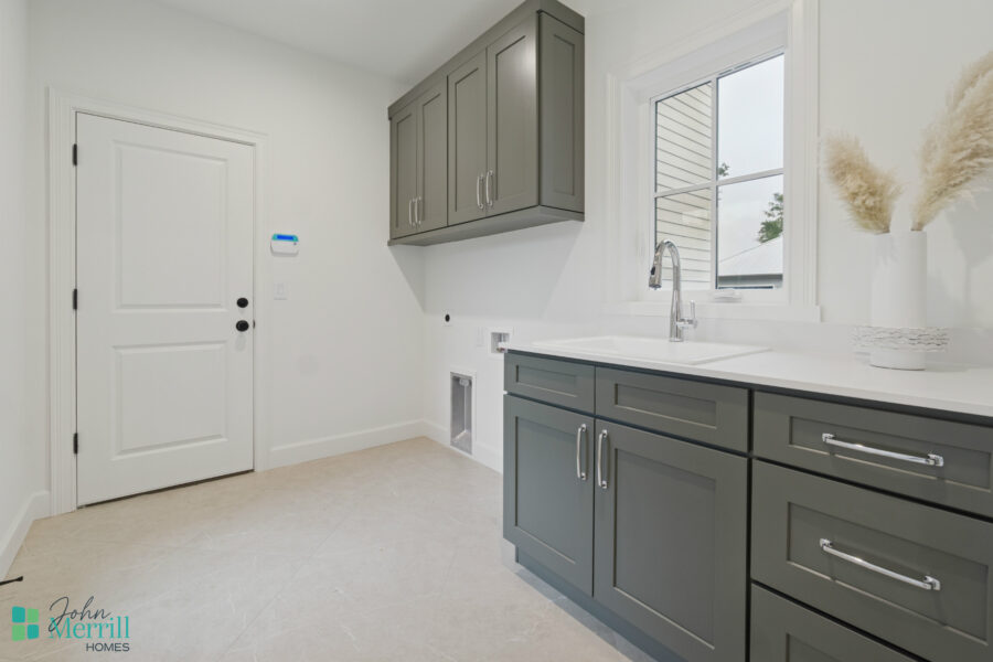 Bright modern kitchen with grey cabinets, white countertops, and a large window, showcasing a stylish and functional space for cooking and entertaining, part of John Merrill Homes' custom home designs.