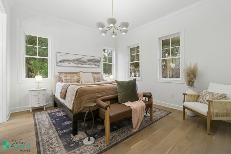 1. Beautifully decorated bedroom with white walls, wooden floors, and large windows offering natural light and a view of greenery outside.