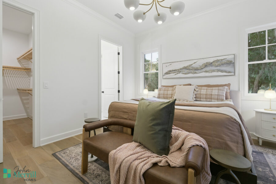 Cozy bedroom with a plush bed, checkered pillows, soft lighting, and modern decor, featuring large windows with a view of greenery, perfect for relaxing and restful nights.