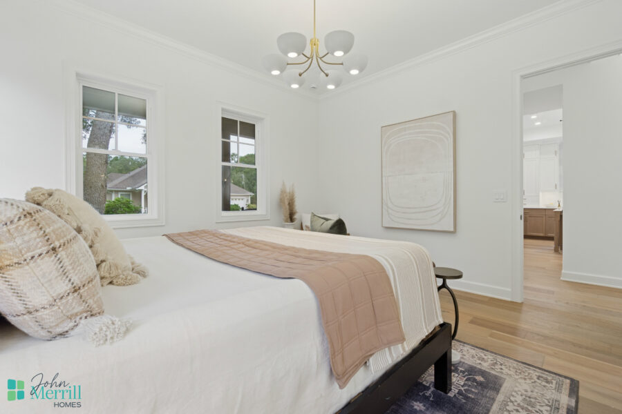 Bright white bedroom with two large windows, minimalist decor, light wood flooring, and a modern ceiling chandelier, showcasing contemporary home interior design by John Merrill Homes.