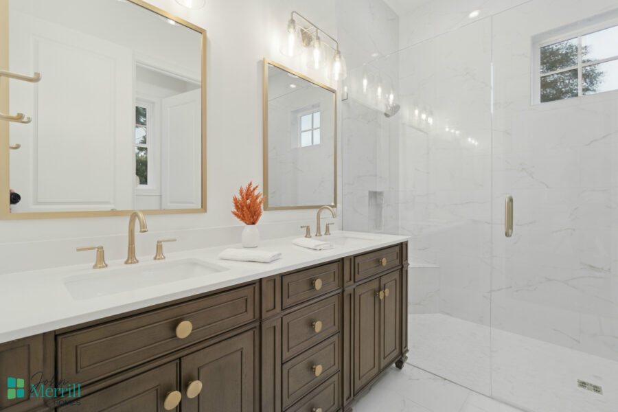 Elegant bathroom vanity with dual sinks, gold fixtures, and a modern marble shower area featuring a glass door and natural light. Perfect blend of functionality and style in home design.