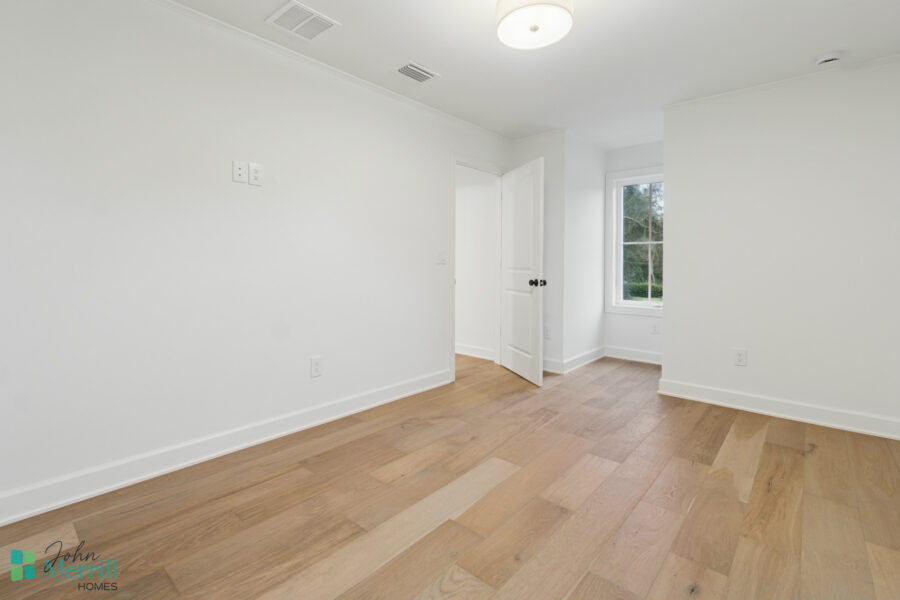 Bright white interior room with natural light, hardwood flooring, and a large window overlooking greenery, creating a spacious and inviting atmosphere.