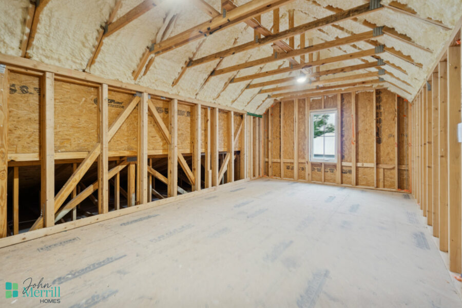 Brightly lit attic space under construction with exposed wooden framing and insulation, showcasing the early stages of custom home building by John Merrill Homes.
