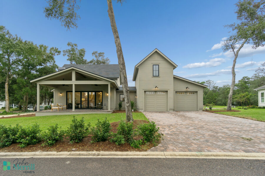 Spacious modern home with a covered porch, attached garage, and lush green landscaping set in a tranquil neighborhood under a bright blue sky.