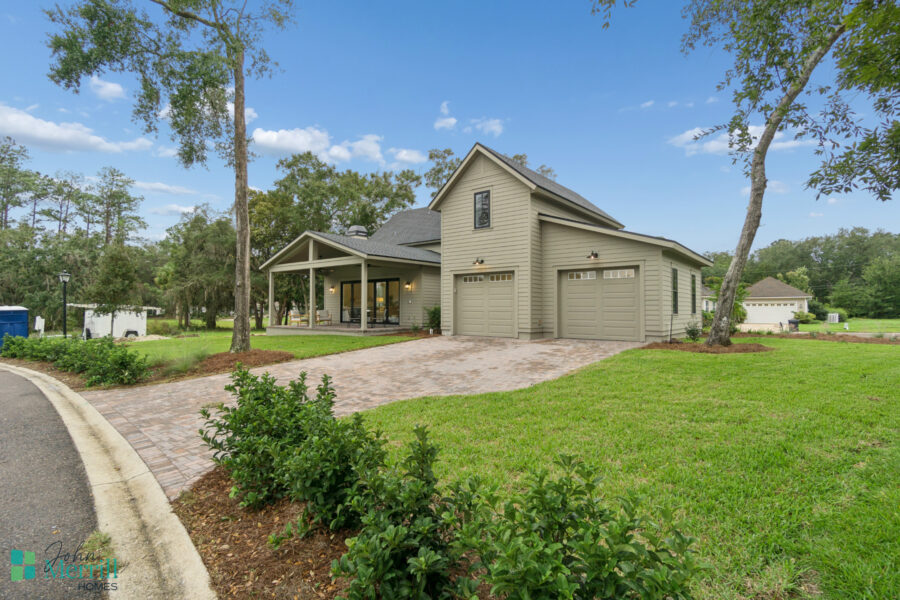 Spacious green front yard with a paved driveway leading to a modern two-story house with a covered porch, surrounded by mature trees and landscaped gardens.