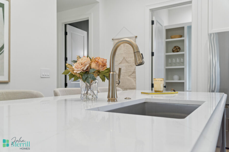 Bright modern kitchen with a white marble countertop, a gold faucet, and a vase of blush-colored flowers, showcasing elegant design and contemporary style in a John Merrill Homes property.