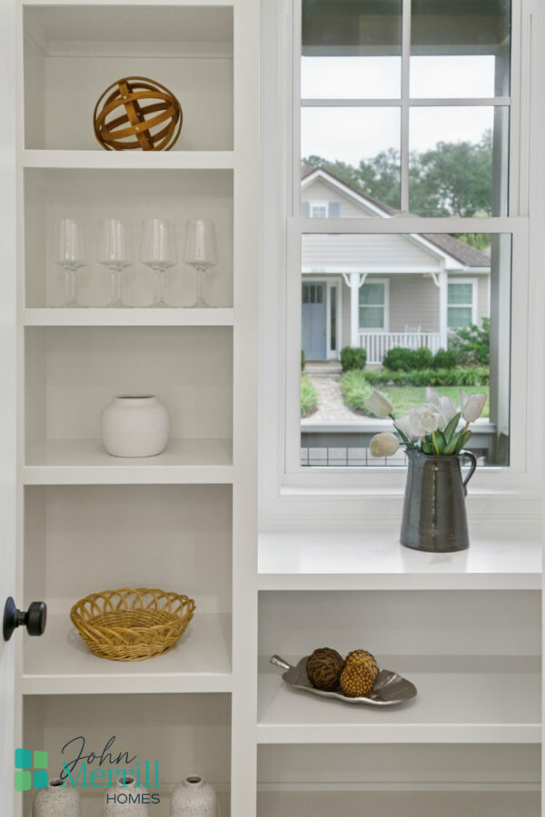Bright white built-in shelves with decorative items and a view of a cozy porch outside, showcasing modern interior design and a welcoming home exterior.