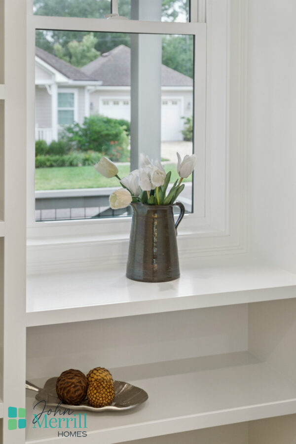 Aesthetic white interior with a view of a cozy suburban neighborhood through a large window, featuring a vase with white tulips on a windowsill. Perfect for modern home decor.