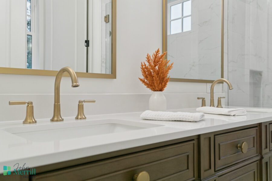 Luxurious bathroom with dual gold faucets, white countertop, large mirror, and elegant decor including a white vase with dried orange plants. Modern, bright, and tastefully designed for comfort.