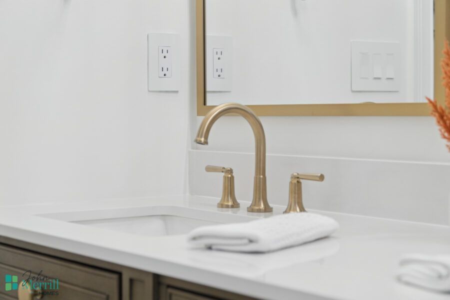 1. Modern bathroom sink with brushed gold faucet, mirror, and white countertop, showcasing elegant home interior design.