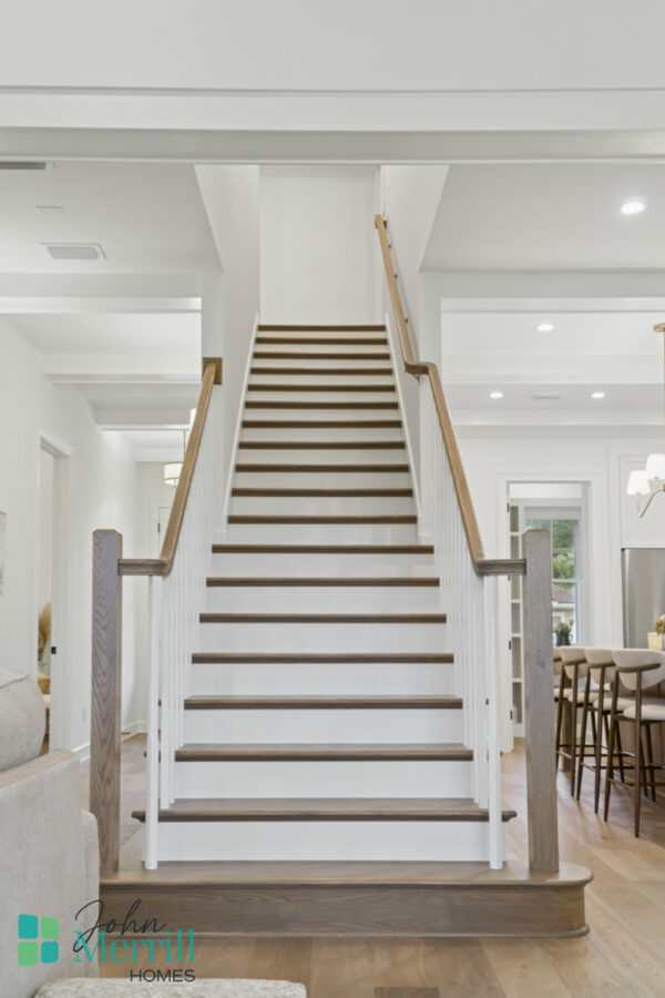 Bright white interior staircase with wooden handrails and steps, leading to the upper floor of a modern home with elegant decor and natural light.